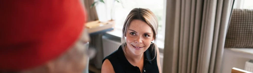 Jonge vrouw met lichtbruin stijl haar glimlacht in een lichte binnenruimte met meubels op de achtergrond