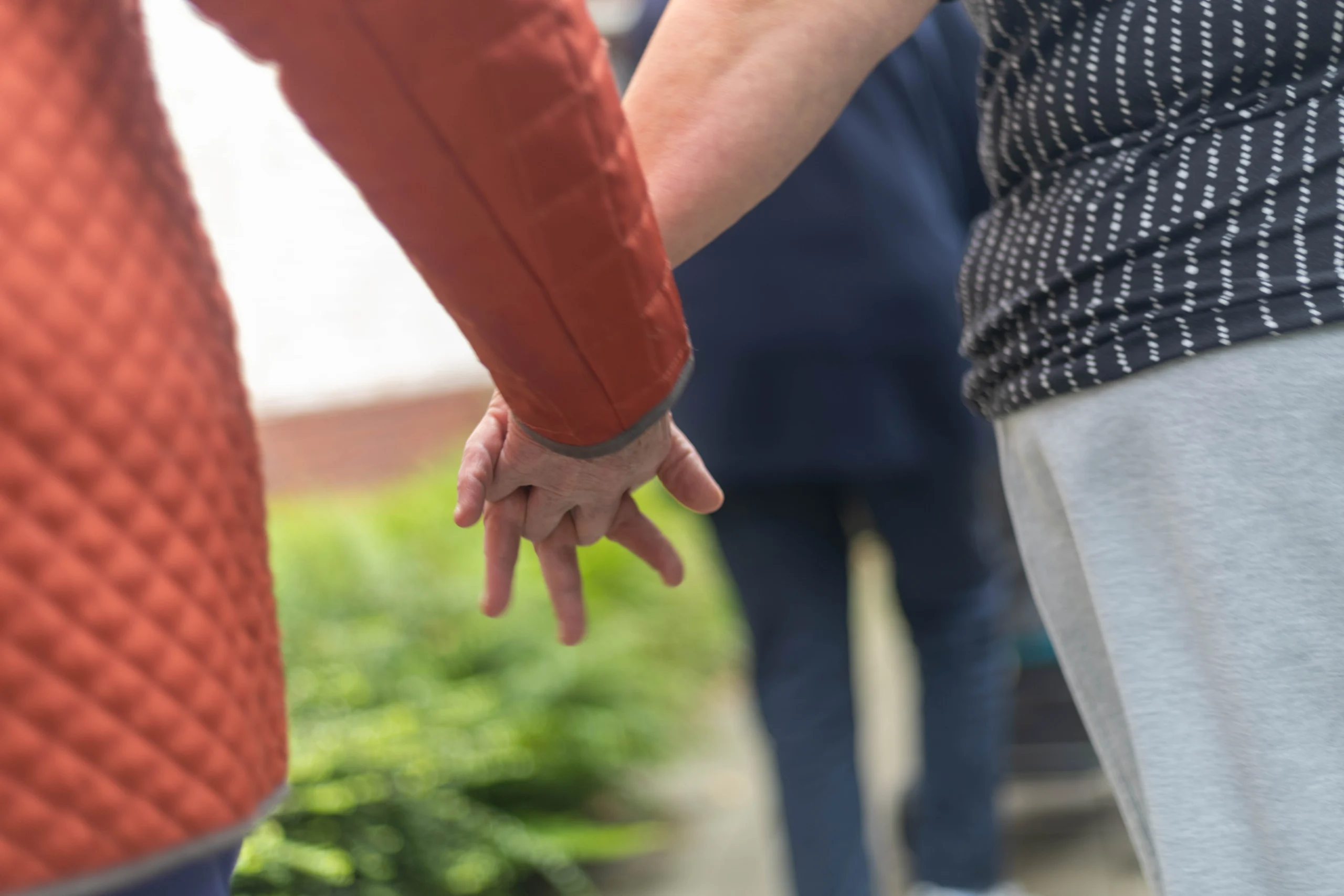 Close-up van twee handen die elkaar vasthouden, één met oranje mouw en één met lichte huid